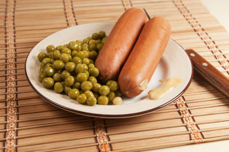Sausages with green peas and mustard in a plate on a table, close-upの写真素材