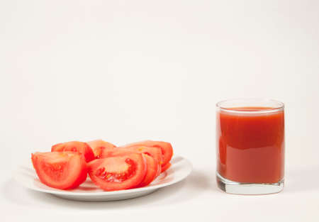 Tomato juice in a glass and tomato pieces on a plateの写真素材