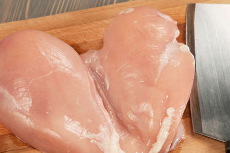 Chicken breast and a knife on a boardの写真素材