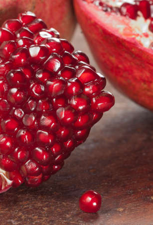 Pomegranate on a dark brown, wooden cutting board. The pomegranate is cut open, with several seeds falling out.の写真素材