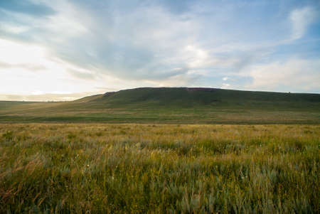 Panorama of cloudy sky and hilly steppe with vegetation under the rays of the setting sun. Selective focusの写真素材