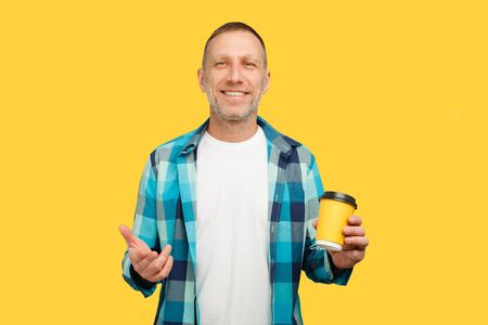 Handsome smiling bearded fifty years old man with coffee or tea to go in a paper yellow cup.