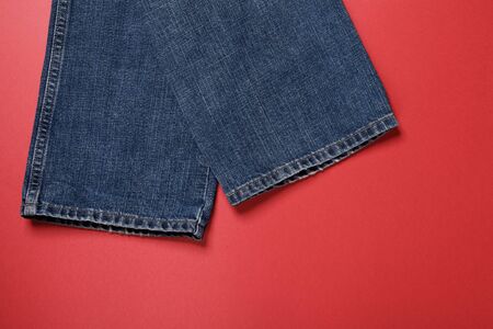 The bottom edge of the trousers of dark blue jeans on a red background.の写真素材