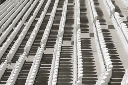 Rows of white empty plastic seats in a stadium.