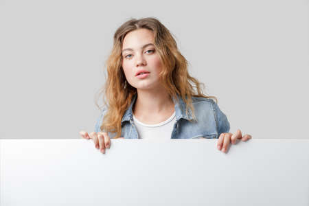 Young caucasian woman holds blank white cardboard. Mockup of the announcement or presentation.の写真素材