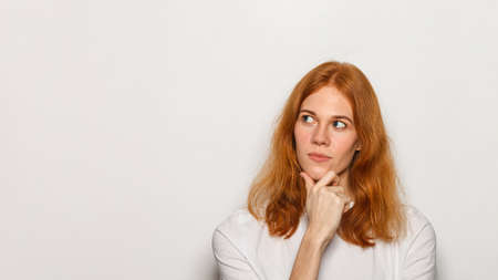 Young thinking woman portrait. Red hair woman wearing white t-shirt isolated over white background.の写真素材