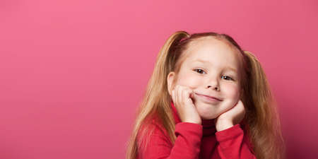 Portrait of a cute smiling 6 years old girl Isolated over pink background. Prop up cheeks with hands.の写真素材