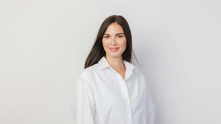 A young business woman in a white shirt poses on a white background. The concept of openness, hospitality, confidenceの写真素材