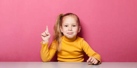 Girl is sitting at the table and shows her index fingers up.の写真素材