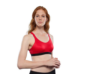 Female athlete poses on a white background. Studio portrait of woman wearing red sporty tank top. Being like hero lookの写真素材