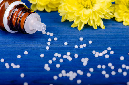 homeopathic globules on a blue  wooden background with yellow flowersの写真素材