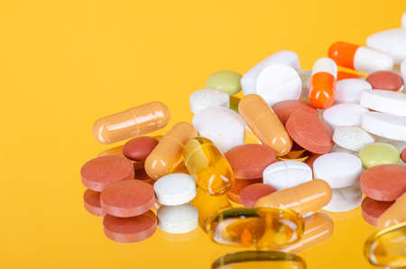various pills on a yellow mirror glass background