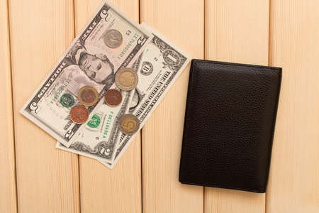 Leather wallet, dollars and coins on the background light wooden table