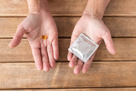 The choice between a condom and a pill . Hands with tablet and a condom on the background of wooden table.の写真素材