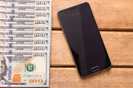 Hundred dollar bill with a smartphone on the table .の写真素材