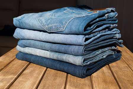 A stack of different pairs of blue jeans on a wooden table . Always in trend .の写真素材