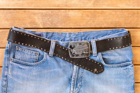 Blue jeans with a black leather strap . On wooden background .の写真素材
