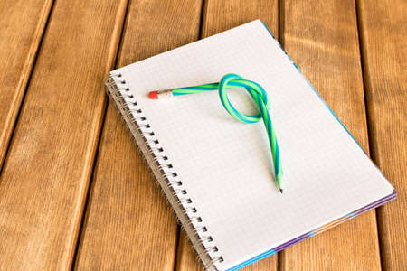 A bent pencil on a notebook . On wooden background .の写真素材