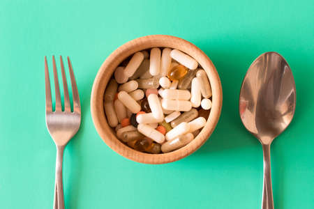 Lots of multicolored pills in a plate on turquoise background . Fork and spoon . The concept of a healthy lifestyle .の写真素材