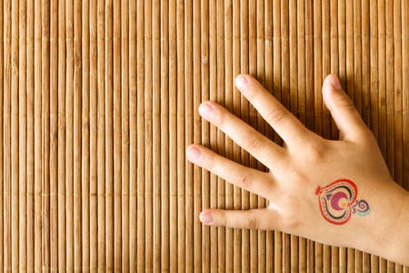 Hand of little girl with baby tattoo on bamboo background