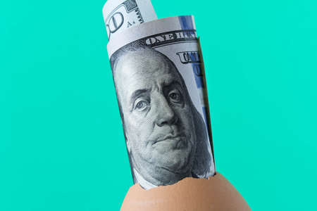 100 dollar bill in an egg shell. On a turquoise background. The concept of saving.の写真素材