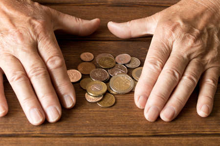 Hands of an elderly man with various coins on a wooden table. The concept of povertyの写真素材