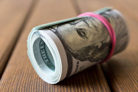 A pack of twisted 100 dollar bills . On a wooden table. Close up.