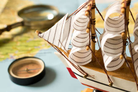 Model sailboat, compass and magnifying glass on map background. Travel concept.