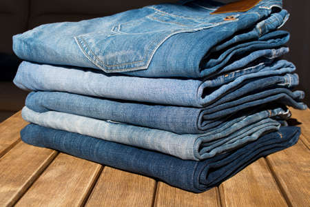 A stack of different pairs of blue jeans on a wooden table . Always in trend .