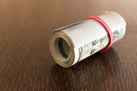 A pack of twisted 100 dollar bills . On a wooden table. Close up.の写真素材