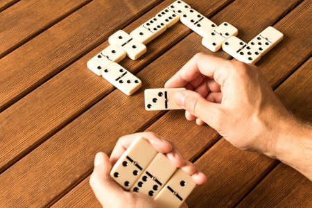 Playing dominoes on a wooden table. Man's hand with dominoes.