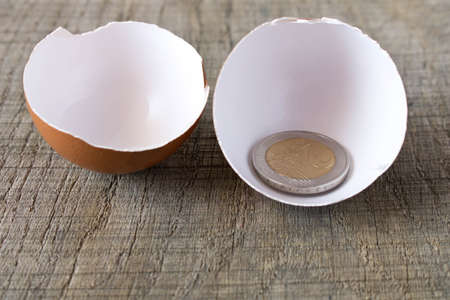 Coin 2 Euro in an egg shell. On an old wooden table. The concept of saving.
