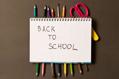 Sign back to school in a notebook. Different school supplies on blackboard background. The concept...