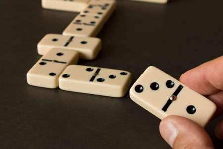A game of dominoes on a dark table . The concept of the game of dominoes. Man's hand with a Domino. Close up.の写真素材