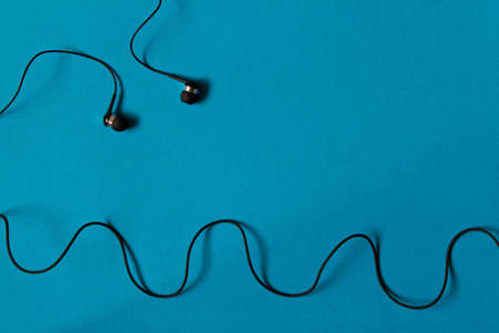 Portable small black earphones. Isolated on blue background.の写真素材