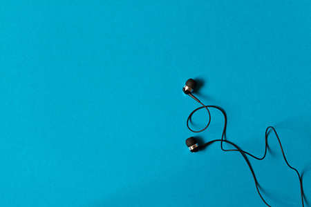 Portable small black earphones. Isolated on blue background. Empty text space.の写真素材