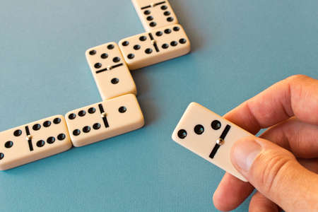 Playing dominoes on a blue background . Man's hand with a Domino. Domino concept.