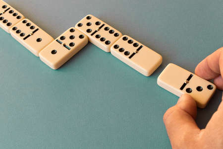 Playing dominoes on a blue background . Man's hand with a Domino. Domino concept.