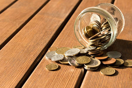 Various coins are scattered on a wooden table. The concept of poverty.