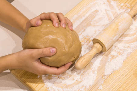 The girl's hands with a dough and rolling pin on a wooden table . Close up. The concept of preparation for Christmas.の写真素材