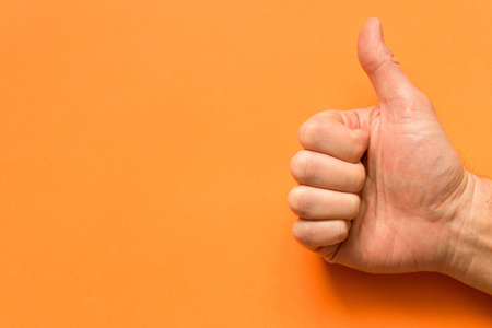 The hand of a man with his thumb up. On an orange background. Empty text spaceの写真素材