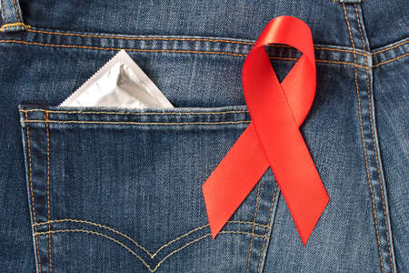 The red AIDS ribbon, a condom in jeans pocket. The concept of reminders about the means of protectionの写真素材