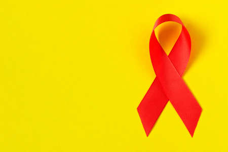 Red aids ribbon.  Isolated on yellow background with empty space for text