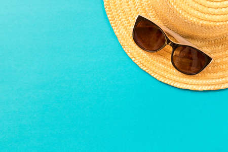 Sunglasses and straw hat on blue background. The concept of summer