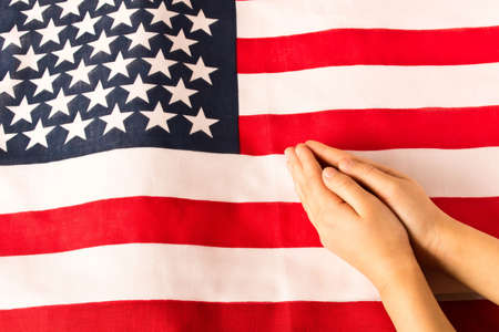 Hands of praying little girl on the background of the American flag. The concept of patriotismの写真素材