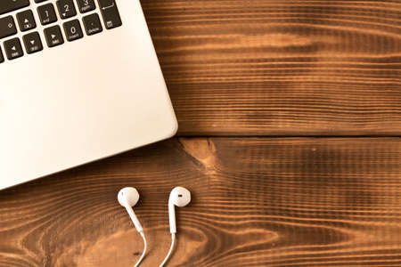 Laptop and  white earphones  on a wooden table. Various office supplies on wooden backgroundの写真素材