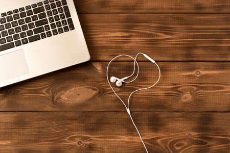 Laptop and  white earphones  on a wooden table. Various office supplies on wooden backgroundの写真素材