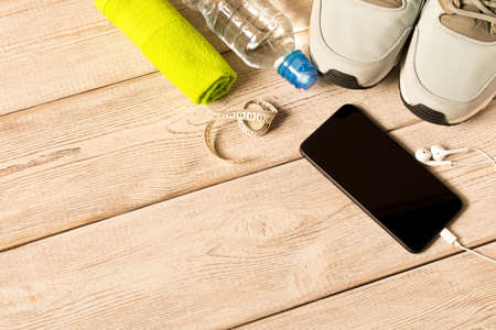 Gray running shoes and fitness accessories on wooden background. Empty text space
