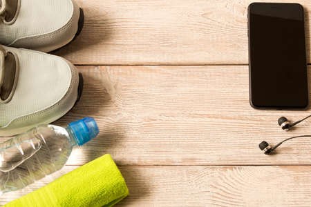 Gray running shoes and fitness accessories on wooden background. Empty text space