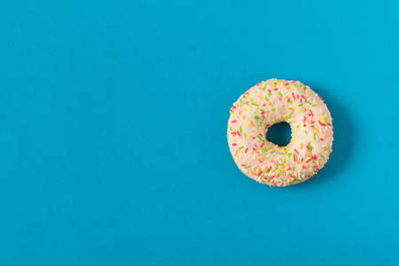 Fresh glazed donut with colorful sprinkles on a blue background
